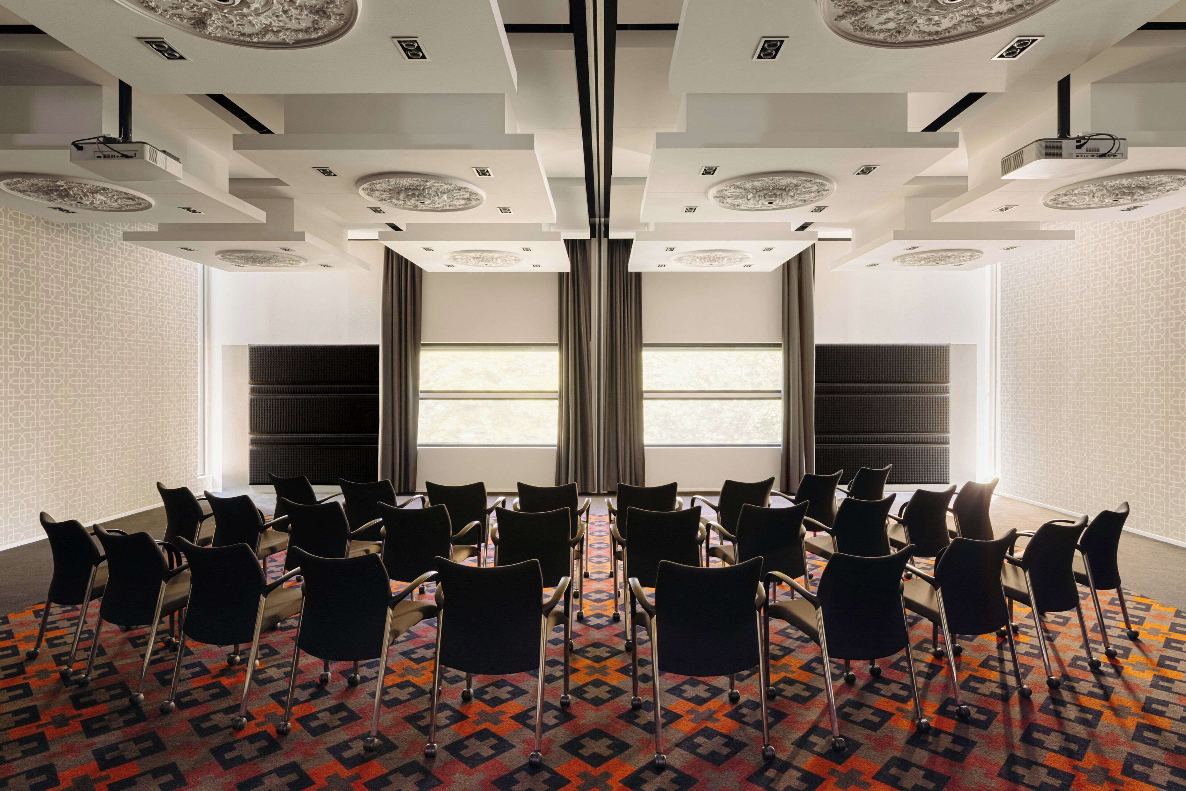 A conference room with rows of chairs, a patterned carpet, and a large window with curtains.