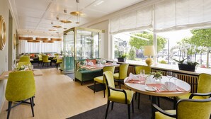 A modern dining area with yellow chairs, a round table, and a glass partition separating the dining space from a seating area. - Hotel Reutemann - Seegarten (Lindau)