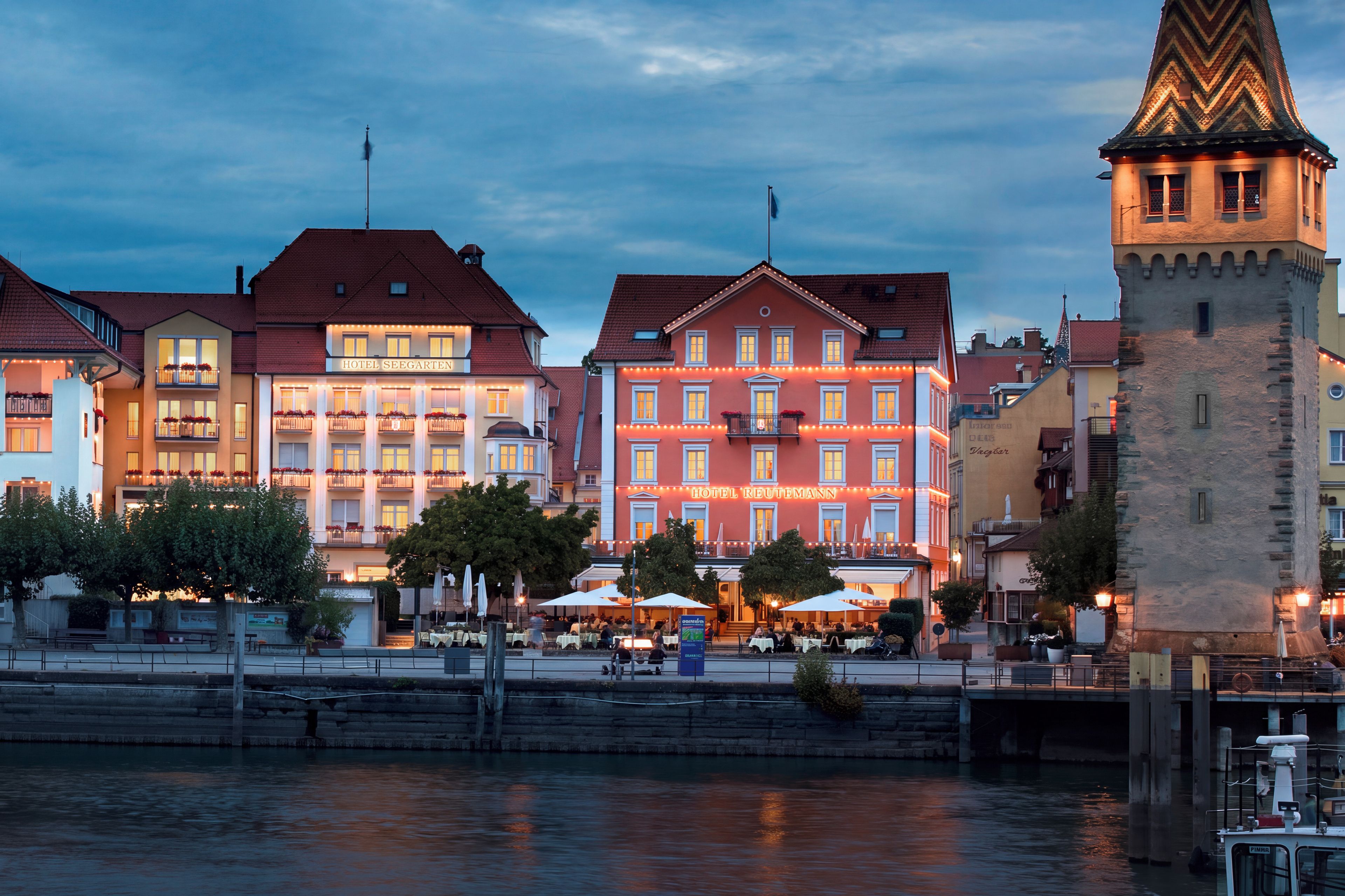 A waterfront hotel with multiple stories, outdoor seating, and a tower structure.