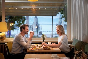 A couple dining at a table with a view of a cityscape and a body of water. - Hotel Seegarten Lindau (Lindau)
