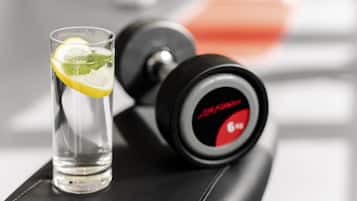 A clear glass with a lemon slice and mint leaves, placed on a black surface next to a dumbbell with a red and black design.