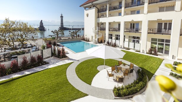 A hotel with a pool, outdoor seating, and a view of a lighthouse and mountains. - Hotel Reutemann - Seegarten (Lindau)