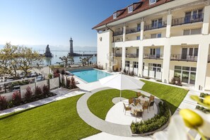 A hotel with a pool, outdoor seating, and a view of a lighthouse and mountains. - Hotel Seegarten Lindau (Lindau)