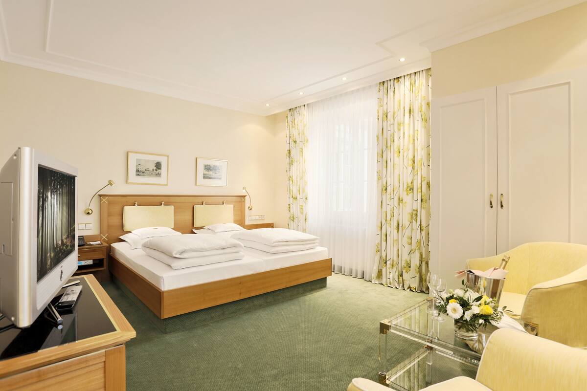 A hotel room with a bed, a television, a desk, a chair, and a glass coffee table.