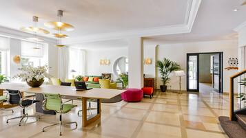 A spacious hotel lobby with a large dining table, comfortable seating, and a staircase leading to other areas.