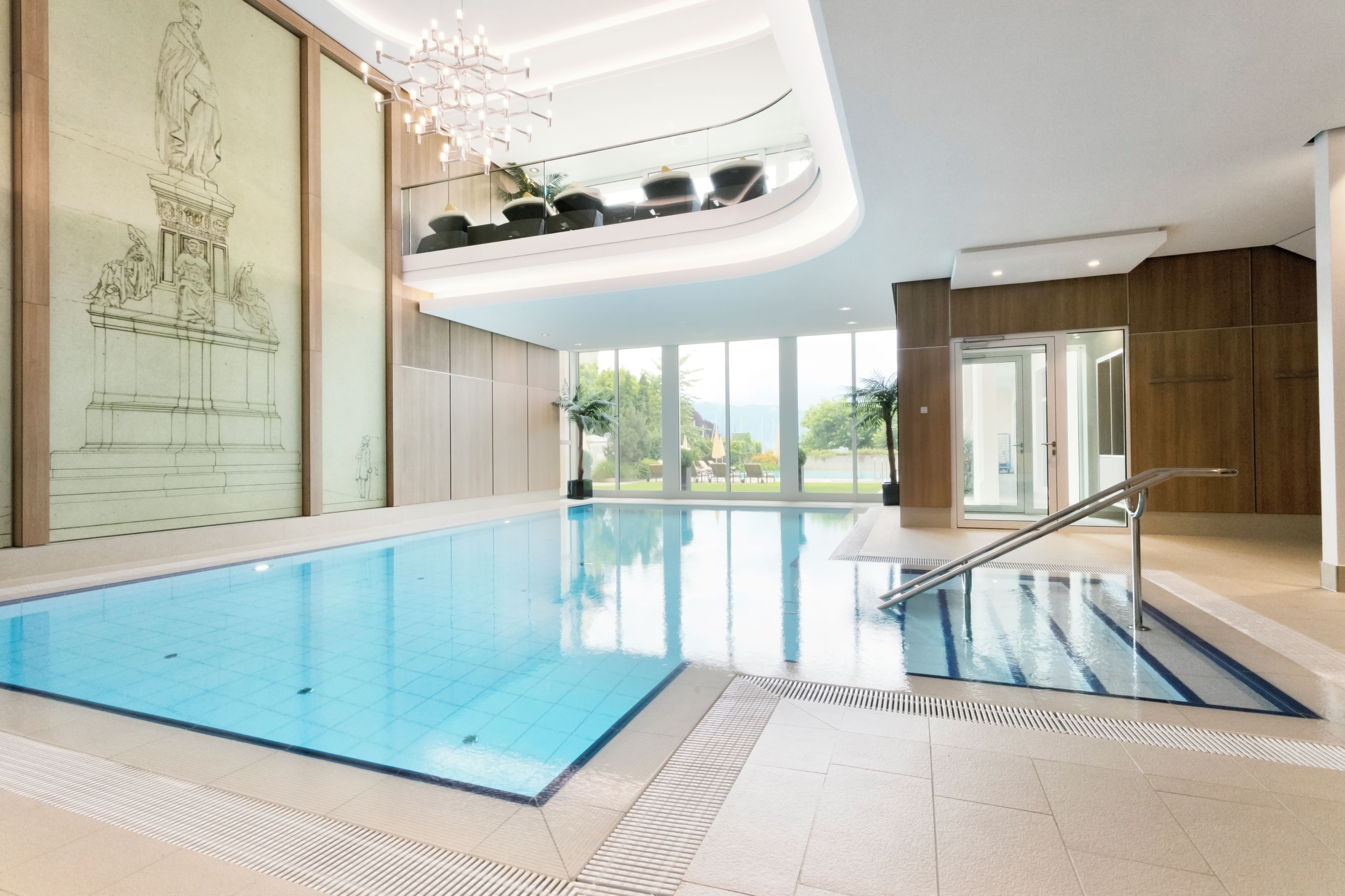 Ein moderner, überdachter Pool mit klarem, blauem Wasser, einer Glasbrüstung und Blick ins Freie durch große Fenster.