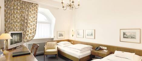 A hotel room with a bed, desk, chair, and a large window with curtains.
