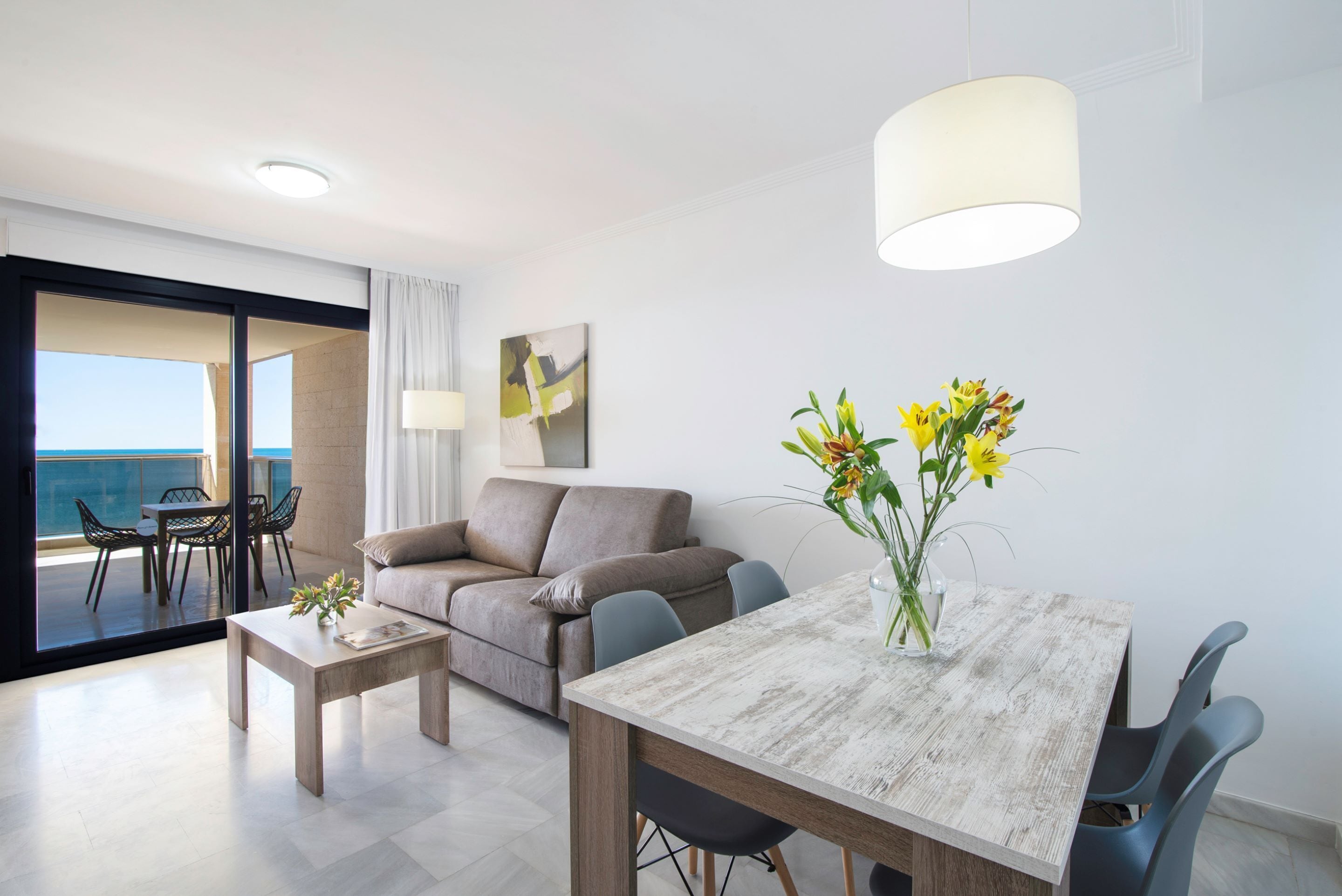 Una sala moderna con sofá, una mesa de comedor y una mesa de centro. Se ve el océano a través de amplios ventanales.