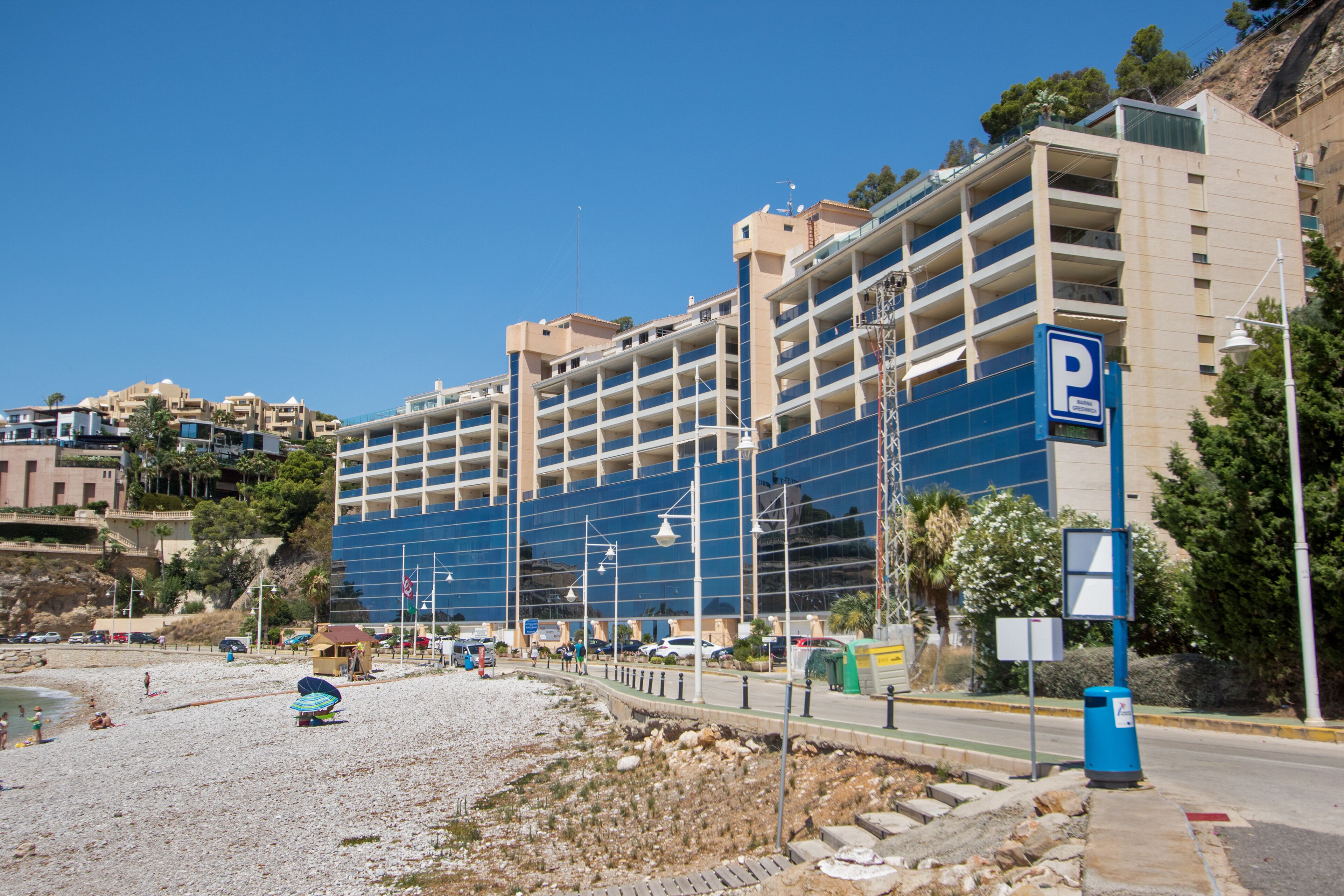 A coastal hotel with multiple floors, a parking sign, and a beach area in the foreground.