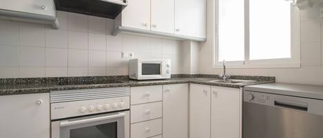 A modern kitchen with white cabinets, a built-in oven, a microwave, and a dishwasher.
