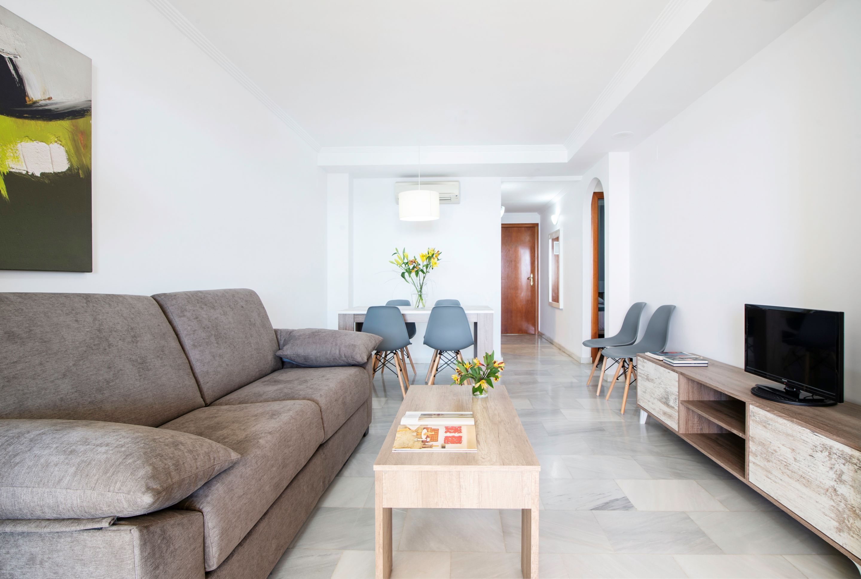 A modern living room with a grey sofa, a wooden coffee table, and a TV on a wooden stand.