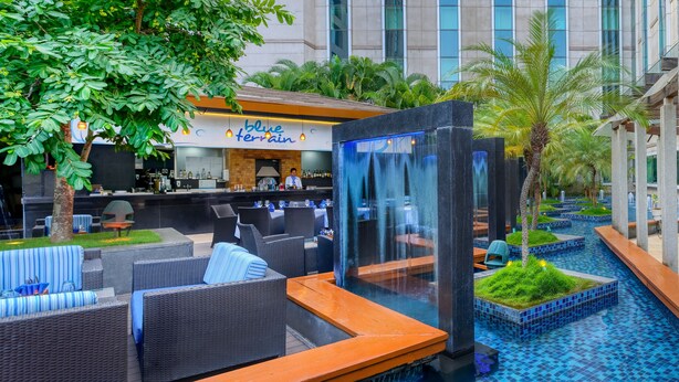 Zona de piscina con mobiliario exterior, bar y cascada.