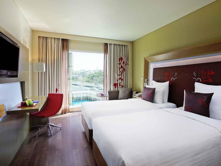 Habitación de hotel con dos camas, un escritorio, una silla, un televisor y vistas a la ciudad.