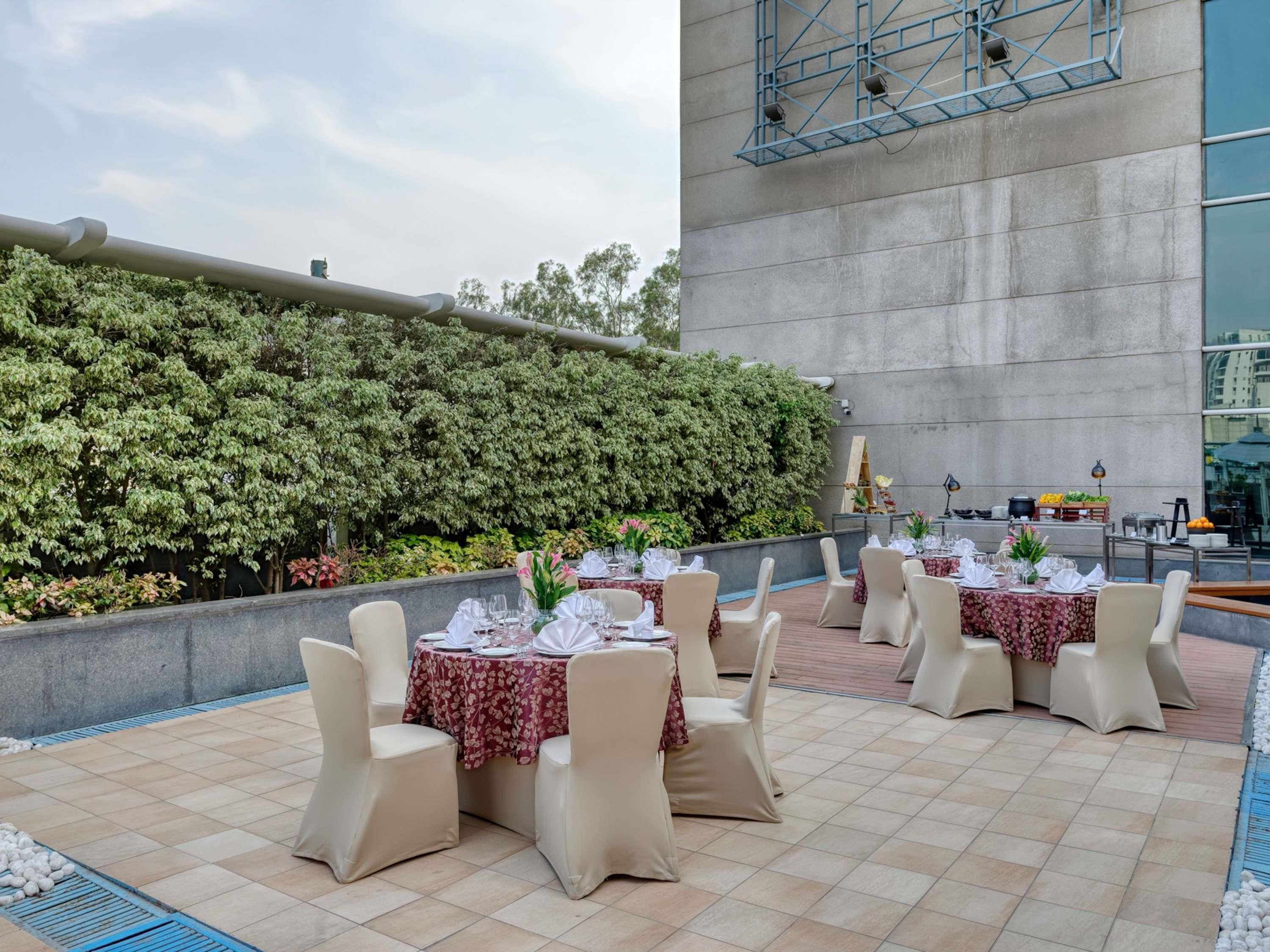 Un espace extérieur aménagé pour les repas, avec des tables dressées, entouré d’un petit muret et d’une haie.