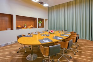 A conference room with a large oval table, chairs, a potted plant, and a curtain. - Novotel Bengaluru Outer Ring Road (Bengaluru)