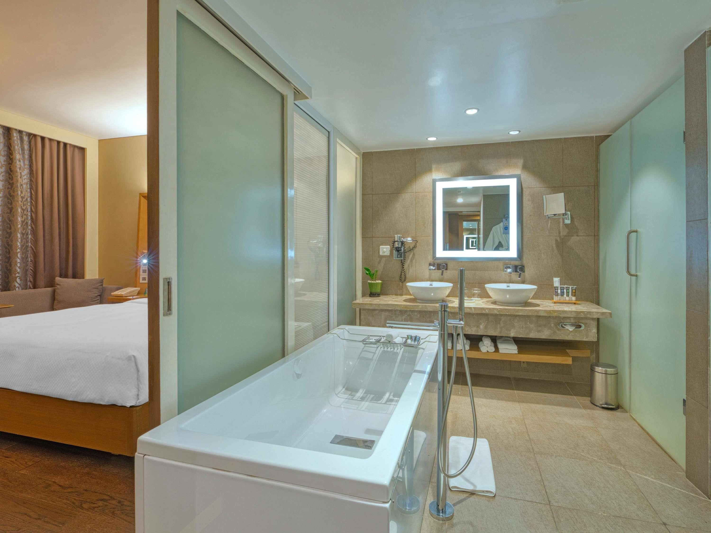 A modern hotel bathroom with a large bathtub, two sinks, and a mirror above the vanity.