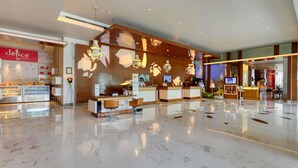 Zona de recepción de un hotel con diseño moderno, que incluye un mostrador de recepción, un área de estar y una barra de panadería.