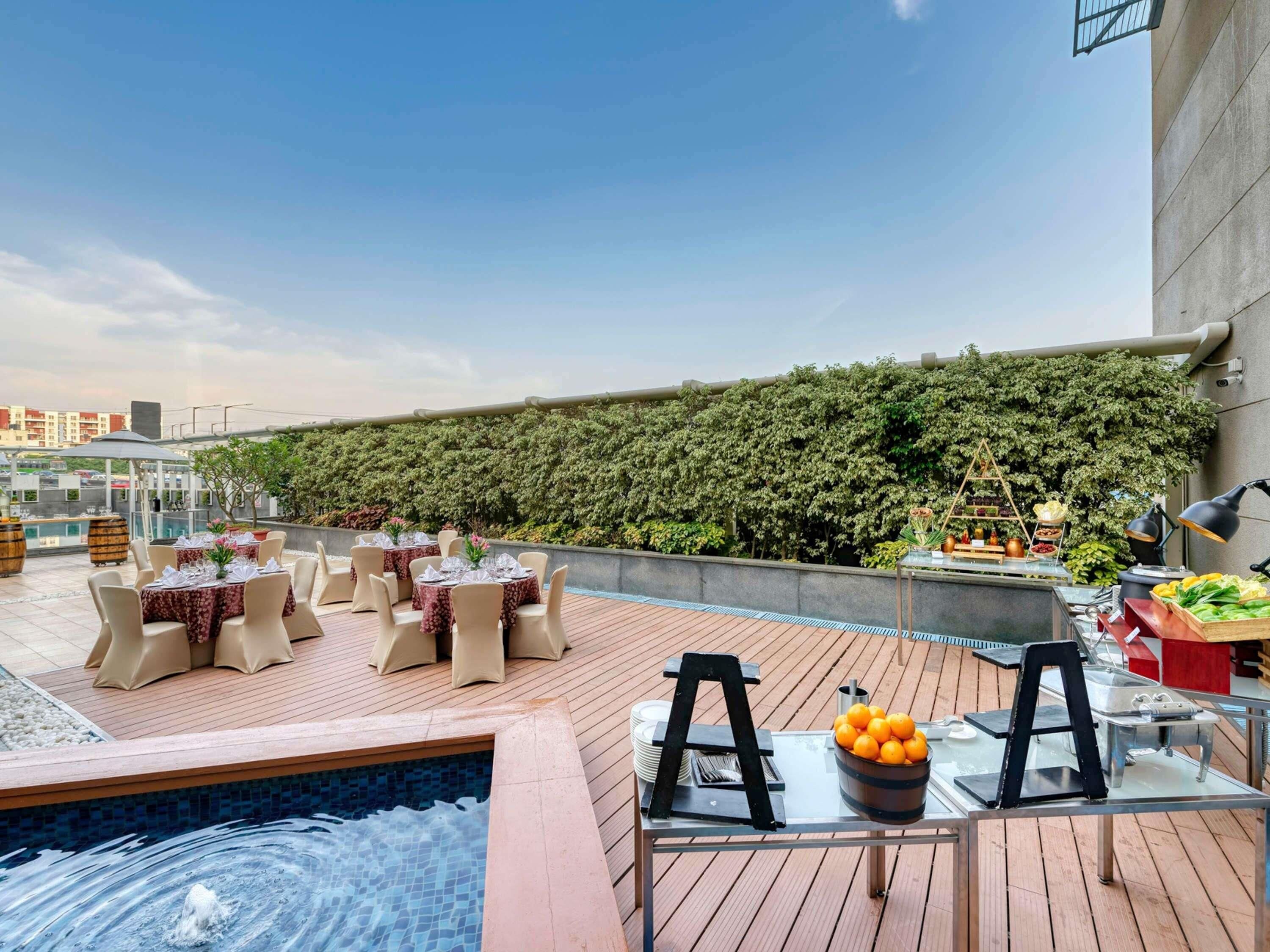 A rooftop dining area with tables set for guests, a small pool, and a wall of greenery.