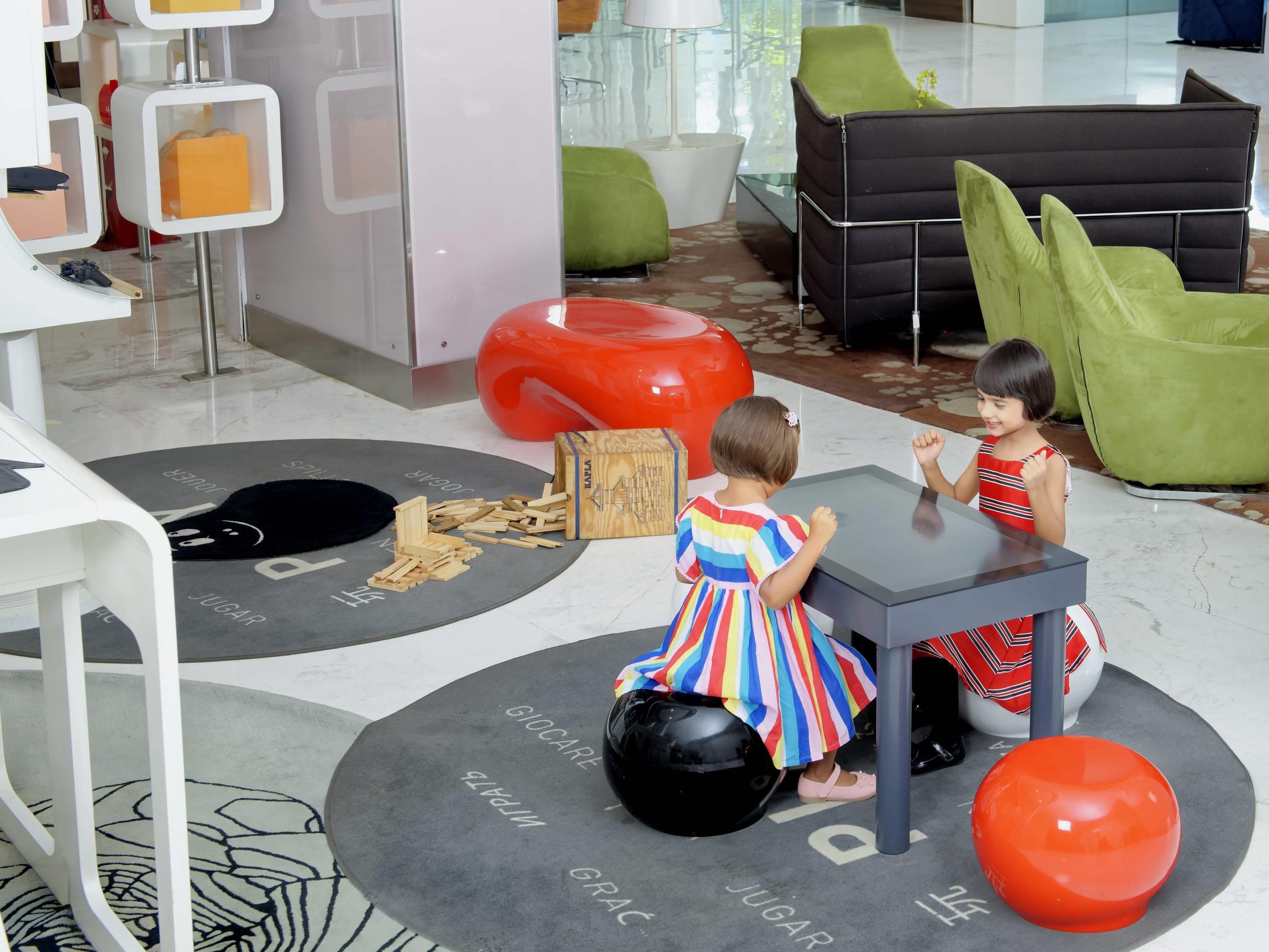 Un área de juegos interior moderna con alfombras de colores, una mesa negra y asientos verdes.