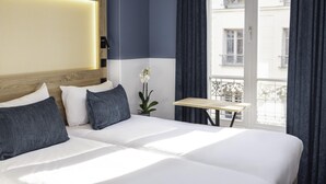 A hotel room with a large bed, a small table, a potted orchid, and a view of buildings through a window. - ibis Styles Paris Montmartre Nord (Paris)