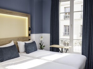 A hotel room with a large bed, a small table, a potted orchid, and a view of buildings through a window. - ibis Styles Paris Montmartre Nord (Paris)
