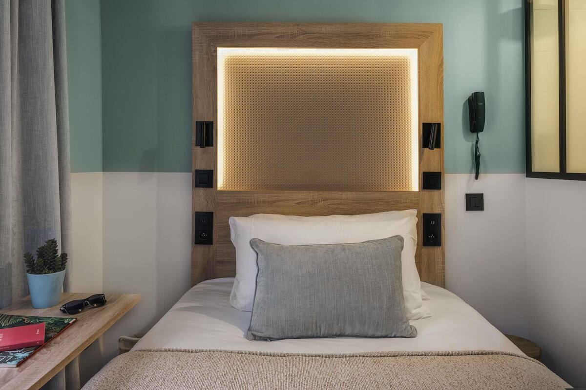 Habitación de hotel con cabecera de madera, una mesita de noche con una planta, un teléfono y un libro.