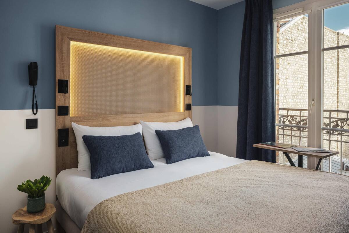 Une chambre d’hôtel avec un lit, un téléphone sur la table de chevet, une petite table avec une plante et une vue par la fenêtre.