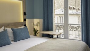 A hotel room with a bed, a bedside table, a window with curtains, and a view of the outside. - ibis Styles Paris Montmartre Nord (Paris)