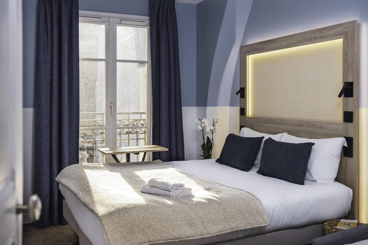 Une chambre d’hôtel avec un lit, une table de chevet, une fenêtre avec des rideaux et une vue sur l’extérieur.