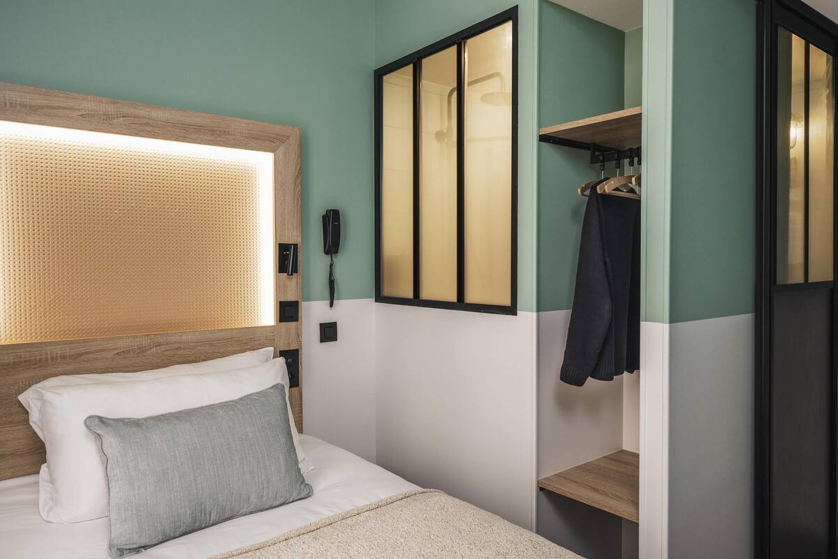 Une chambre d’hôtel équipée d’un lit, d’un téléphone sur la table de chevet, d’un porte-manteau et d’un miroir.