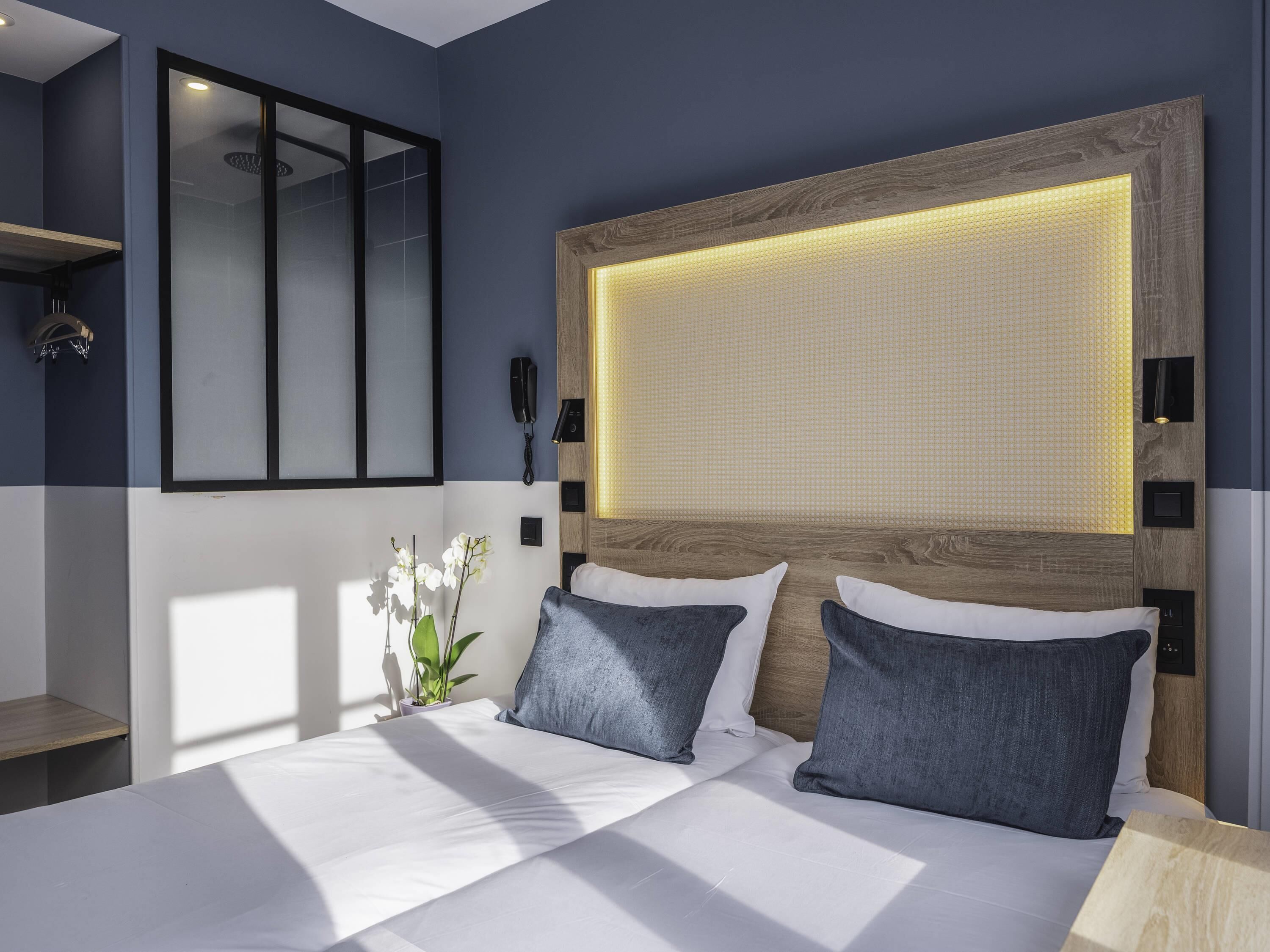 Een moderne hotelkamer met een groot bed, nachtkastje, spiegel, telefoon en een wandlamp.