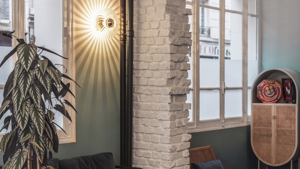 A cozy living area with a sofa, a coffee table with magazines, a hanging light fixture, and a large plant. - ibis Styles Paris Montmartre Nord (Paris)