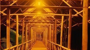 A wooden walkway with a series of arches and railings, leading towards a light source at the end.