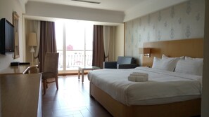 A hotel room with a large bed, a desk, a chair, a TV, and a balcony with curtains. - Discovery Hotel (Phnom Penh)