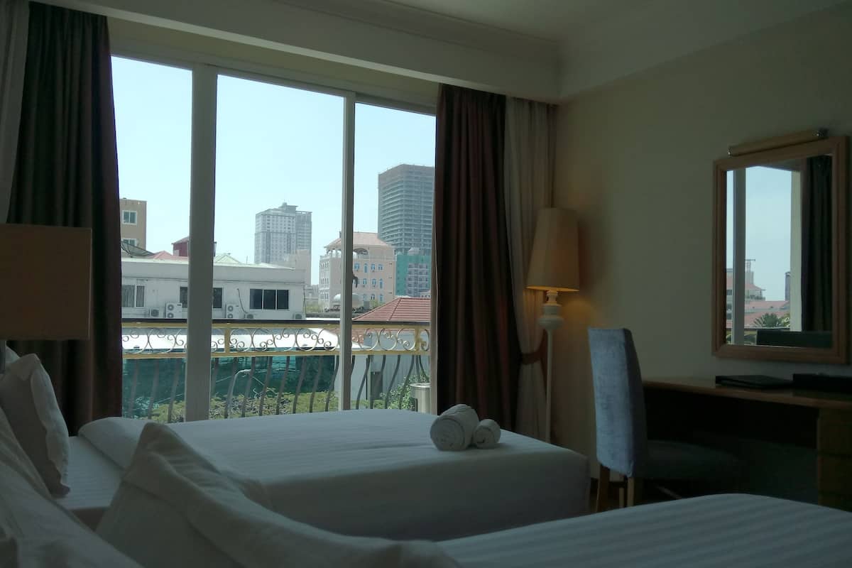 A hotel room with two beds, a desk, a chair, a lamp, and a large window with a city view.