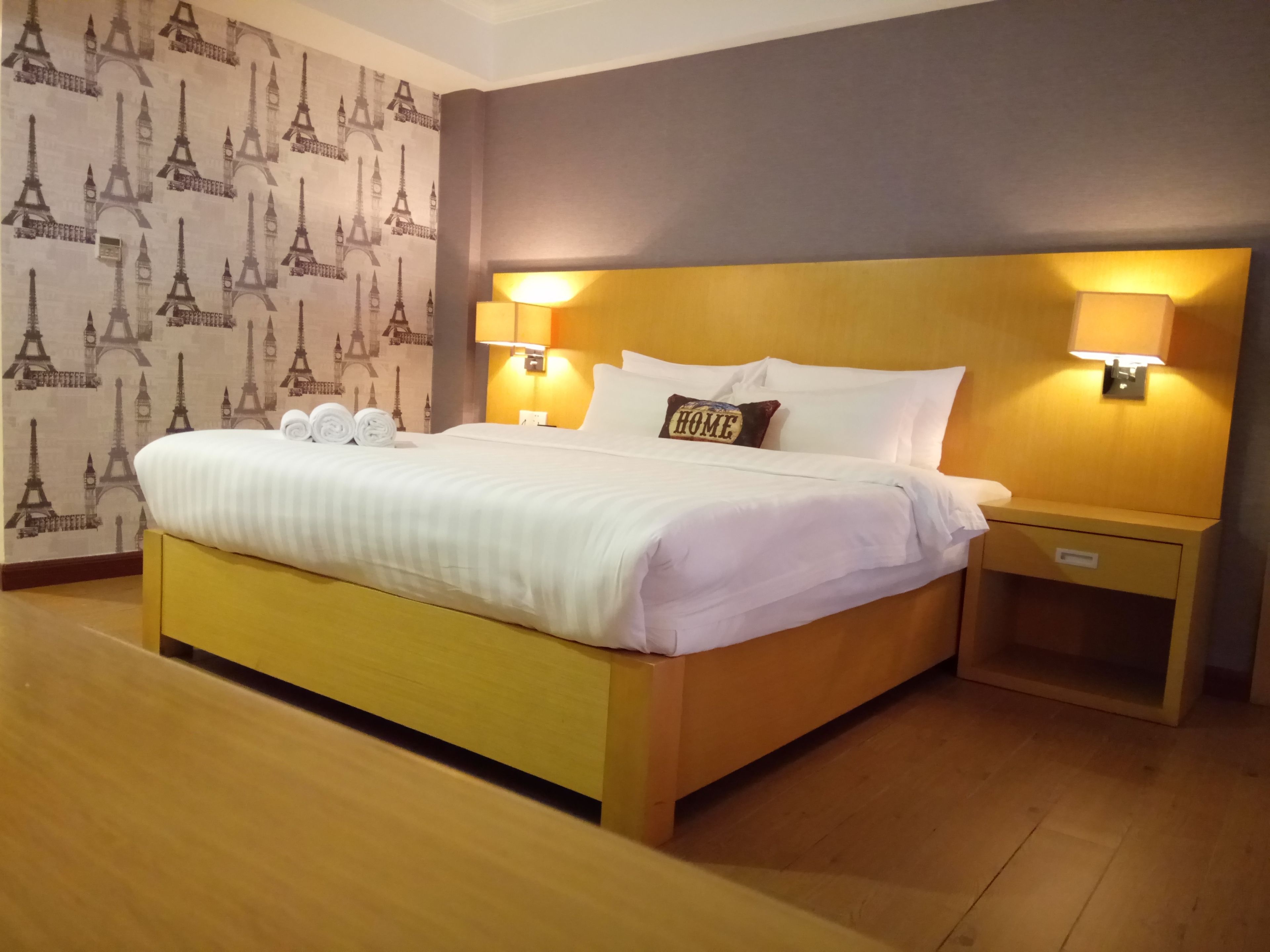 Una habitación de hotel con una cama grande, dos lámparas de noche, una mesita de noche y un papel tapiz con motivos de la Torre Eiffel.