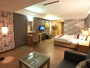 A hotel room with a bed, a desk, a chair, a TV, and a small table with a vase. - Discovery Hotel (Phnom Penh)