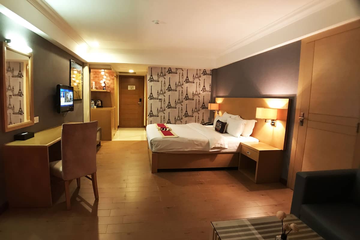 A hotel room with a bed, bedside tables, a desk, a chair, and a TV.