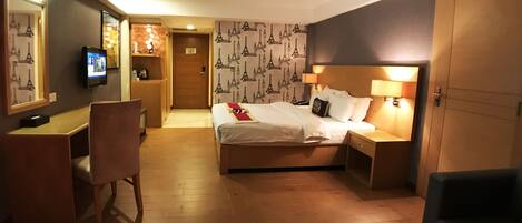 A hotel room with a bed, bedside tables, a desk, a chair, and a TV.