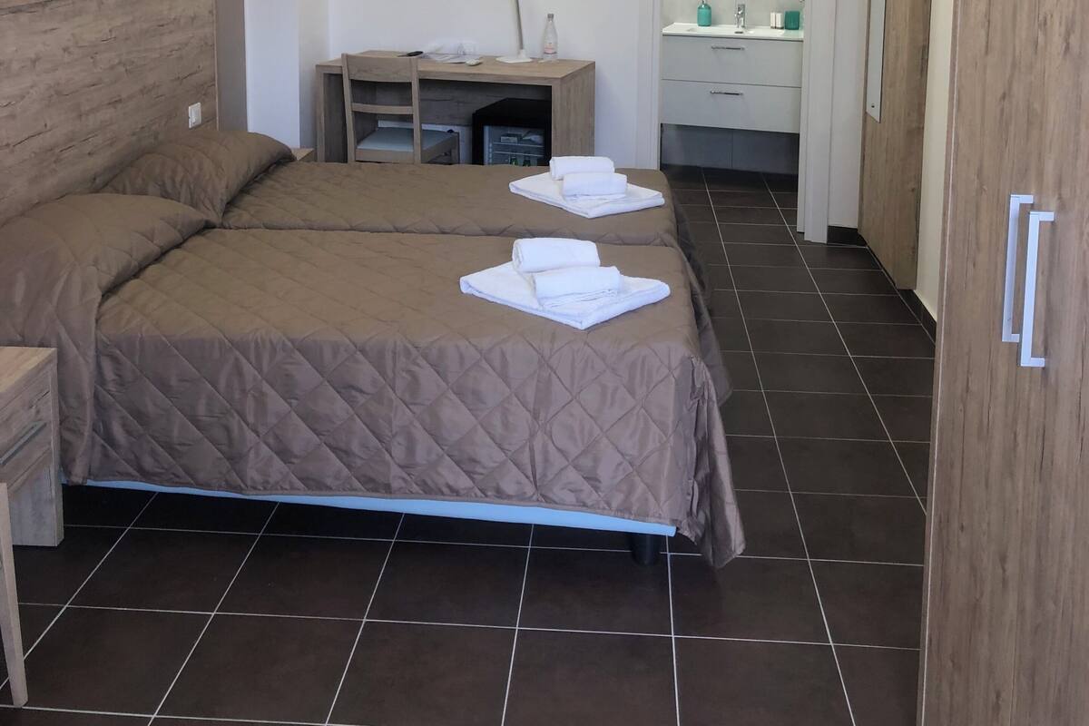 A hotel room with two beds, a desk, a mirror, and a wardrobe.