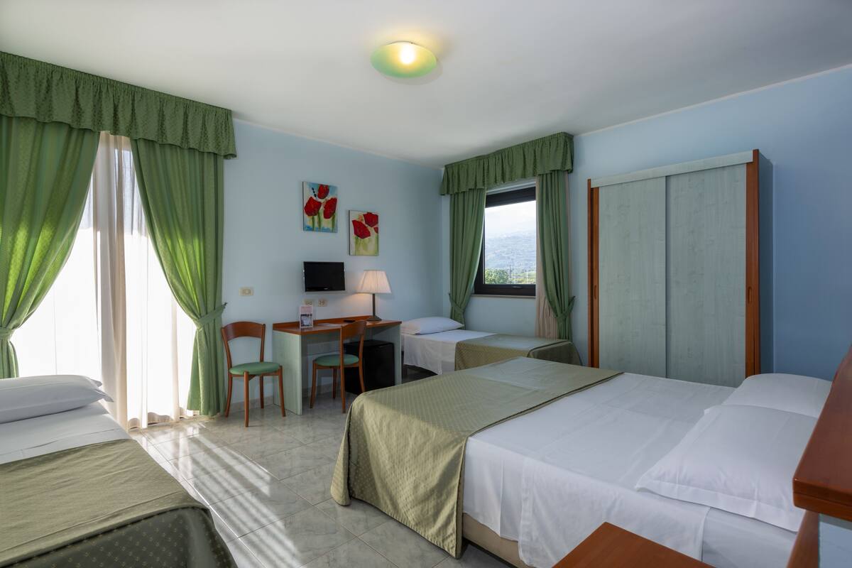 A hotel room with two beds, a desk with a chair, a TV, and a window with curtains.