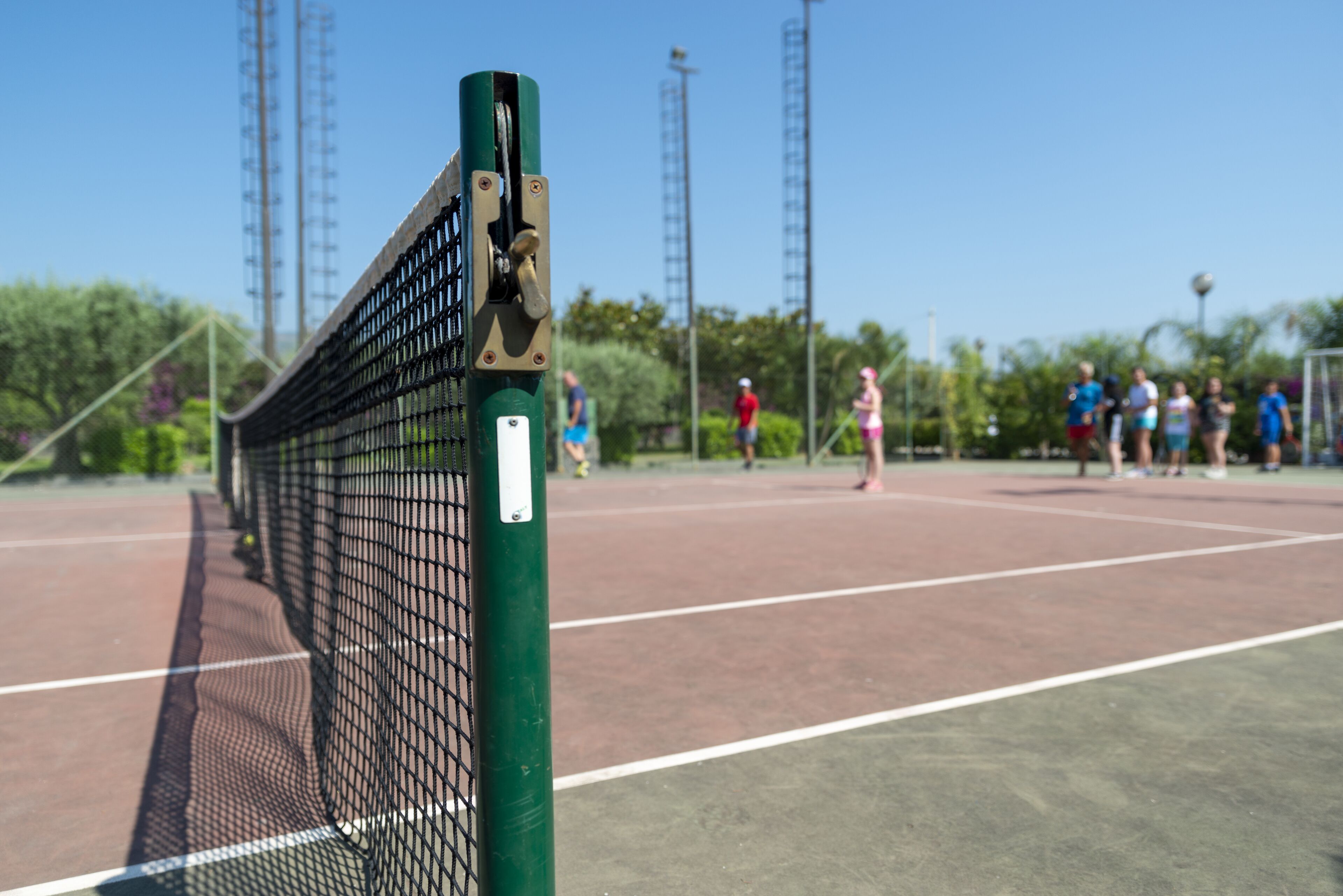 A tennis court with a net in the foreground and people playing in the background.