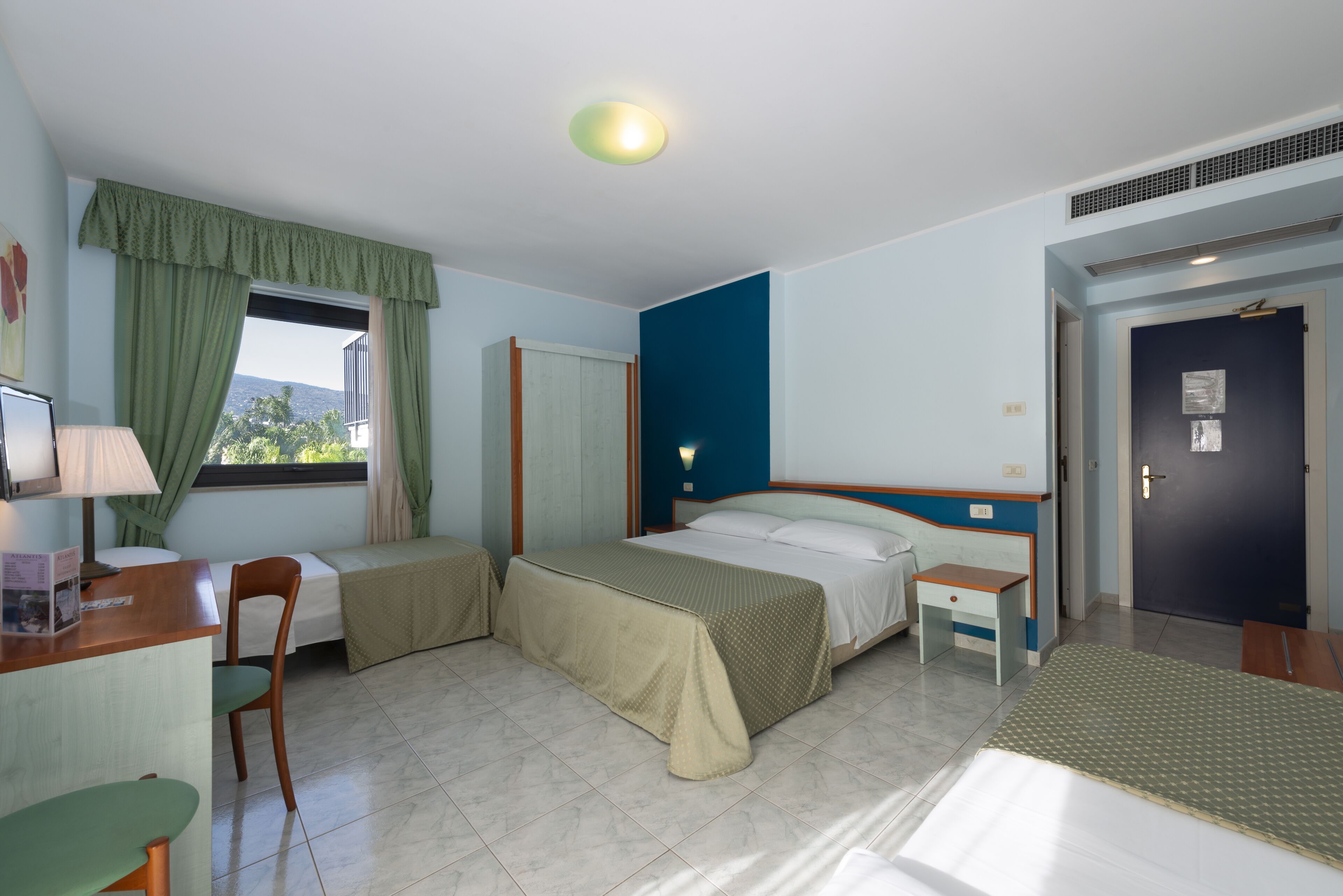 Ein Hotelzimmer mit einem Bett, einem Schreibtisch, einem Stuhl, einem kleinen Tisch und einem Fenster mit Vorhängen.