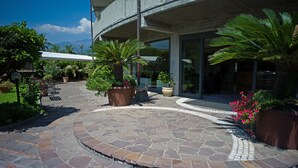 A courtyard with stone flooring, potted plants, outdoor seating, and a building entrance. - Atlantis Palace Hotel (Mascali)