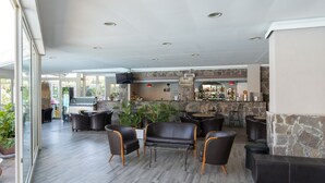 A modern bar area with seating, a stone wall, and a television. - Atlantis Palace Hotel (Mascali)