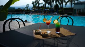 A poolside table with drinks and snacks, overlooking a pool with palm trees and lounge chairs. - Atlantis Palace Hotel (Mascali)