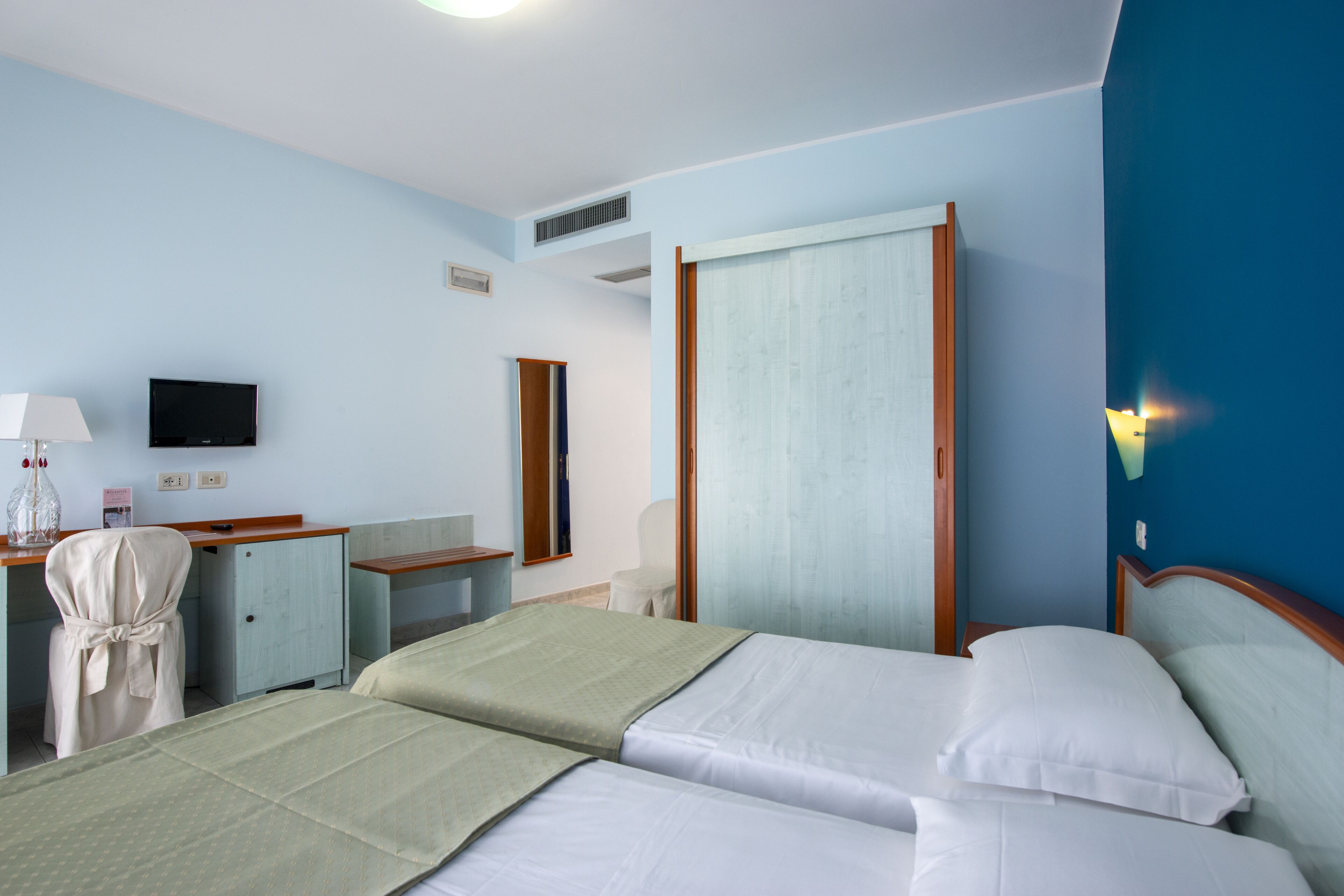 A hotel room with two beds, a desk with a chair, a television, and a large window with curtains.