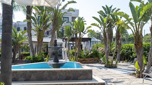 A pool area with a fountain, surrounded by palm trees and a building in the background. - Atlantis Palace Hotel (Mascali)
