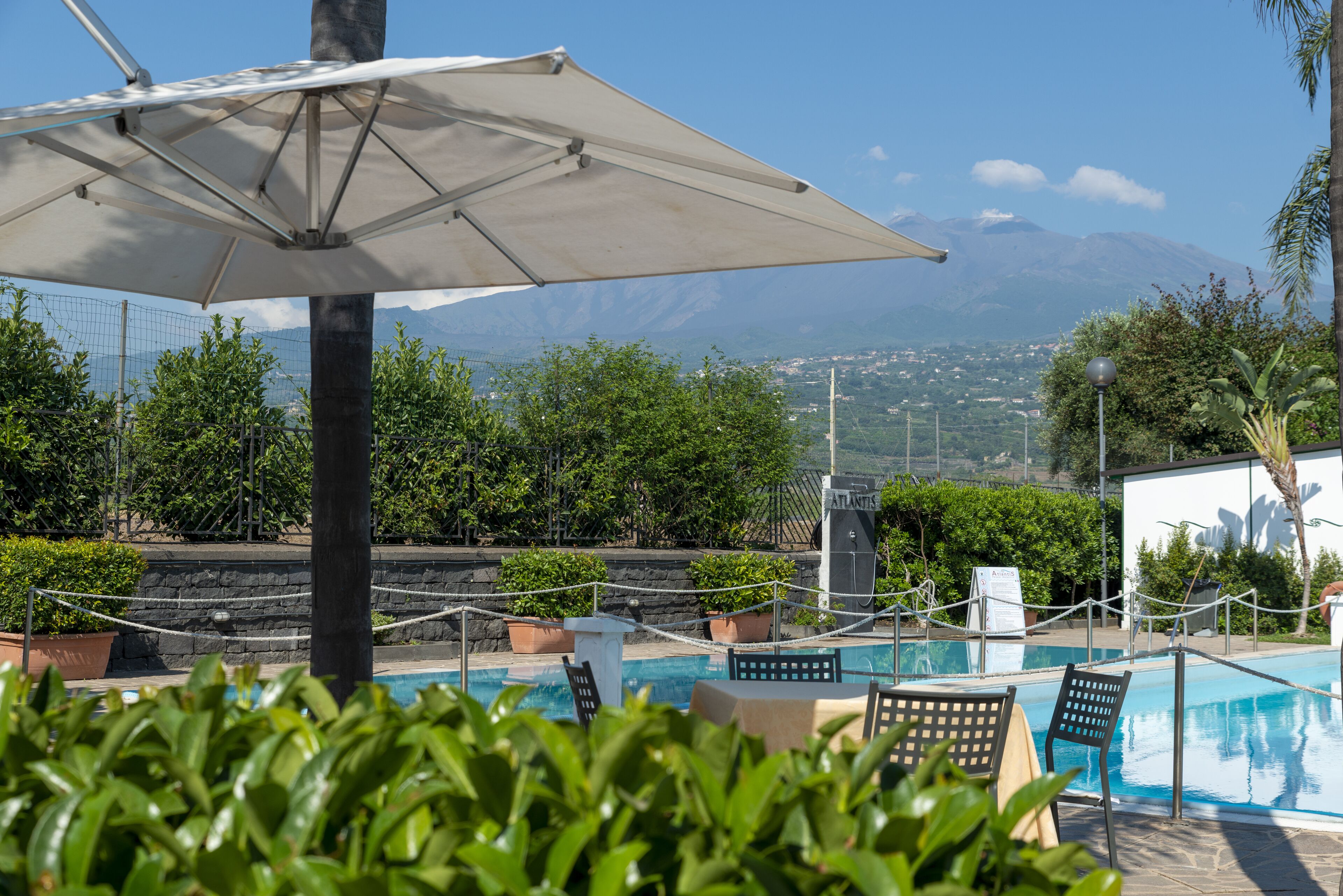 A pool area with a view of mountains, surrounded by greenery and a white umbrella.