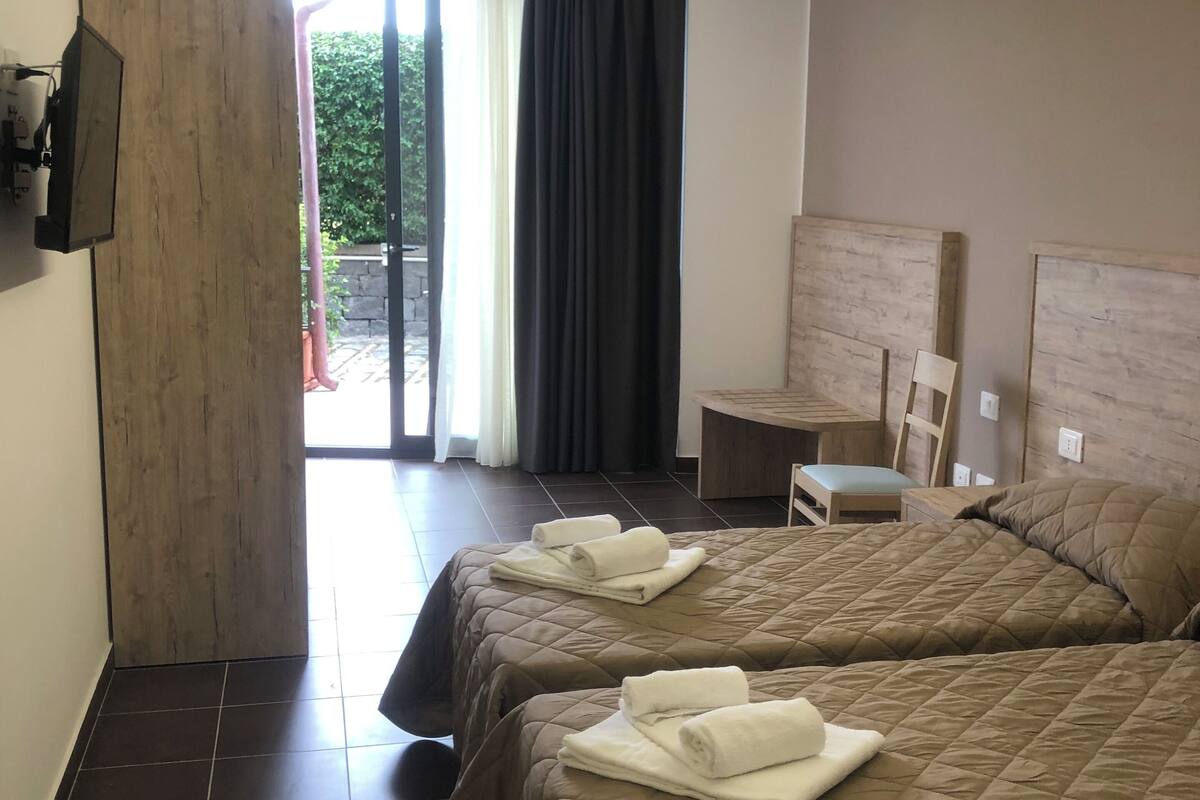 A hotel room with two beds, a small table, a chair, and a TV mounted on the wall.